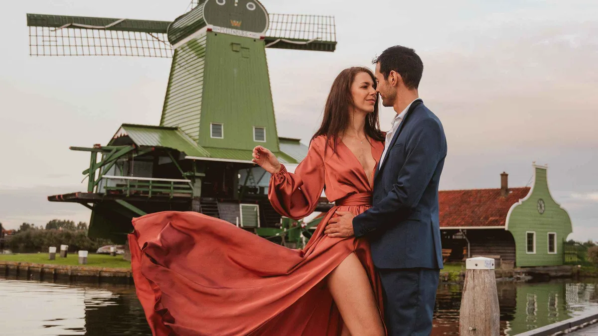 Couple photographed in front of the green windmills of Zaanse Schans on an Amsterdam photoshoot day trip, Netherlands